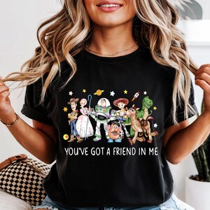 May include: Black t-shirt featuring a colorful graphic of Toy Story characters, including Woody, Buzz Lightyear, and Rex. The text "YOU'VE GOT A FRIEND IN ME" is printed below the characters. The shirt is a casual wear item.
