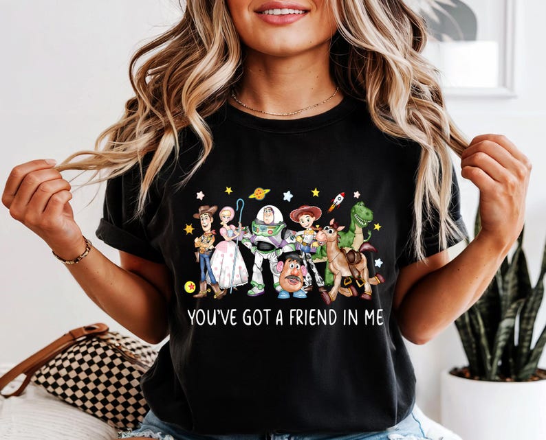 May include: Black t-shirt featuring a colorful graphic of Toy Story characters, including Woody, Buzz Lightyear, and Rex. The text "YOU'VE GOT A FRIEND IN ME" is printed below the characters. The shirt is a casual wear item.