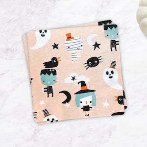 May include: A stack of pink paper napkins with a Halloween theme. The napkins feature a repeating pattern of ghosts, mummies, witches, spiders, and bats in black, white, and blue on a pink background.