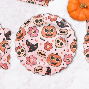 May include: Pink paper plates with a Halloween theme. The plates feature a repeating pattern of pumpkins, skulls, flowers, bats, stars, and the word "Boo!"
