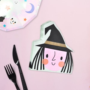 Puede incluir: Un paquete de servilletas de papel con una ilustración de una bruja. La bruja lleva un sombrero negro con una banda dorada y tiene una cara rosa con ojos negros y una sonrisa. Las servilletas son perfectas para una fiesta de Halloween.