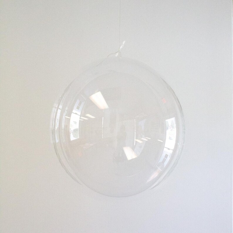 Op de afbeelding: Een doorzichtige plastic bubbelballon die aan een touwtje hangt. De ballon is opgeblazen en lijkt rond te zijn.