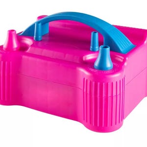 Könnte beinhalten: Eine leuchtend pinkfarbene elektrische Luftballonpumpe mit blauem Griff und Düsen. Das rechteckige Gerät hat ein geriffeltes Design an den Seiten und ist zum Aufblasen von Luftballons bestimmt. Der Griff und die Düsen sind in einem kontrastierenden Blau gehalten.