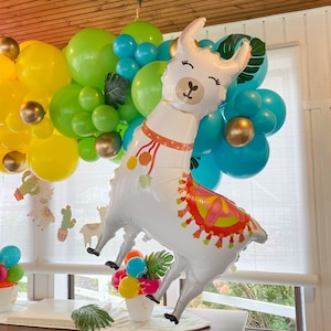 May include: A white llama balloon with a colorful patterned saddle, surrounded by yellow, green, and blue balloons. The llama balloon has a friendly face with closed eyes and a small nose.