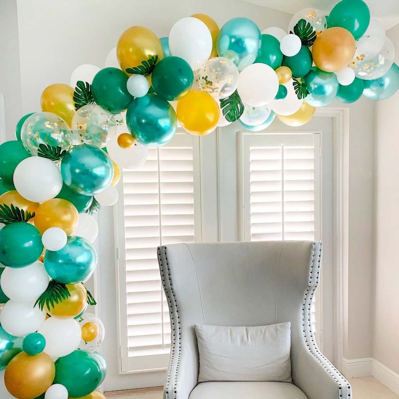 Op de afbeelding: Een groene, gouden en witte ballonboog met tropische bladeren. De boog is gemaakt van ballonnen in verschillende maten en texturen.