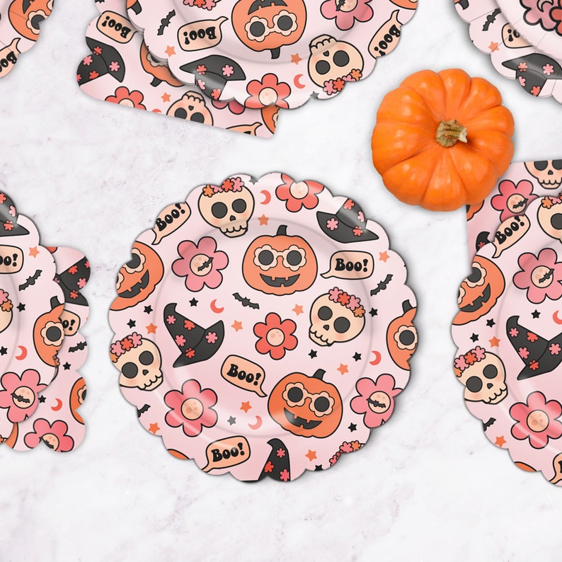 May include: Pink paper plates with a Halloween theme. The plates feature a repeating pattern of pumpkins, skulls, flowers, bats, stars, and the word "Boo!"