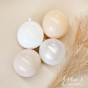 May include: Four balloons in various shades of beige, white, and cream. The balloons are arranged in a semi-circle on a light brown background.