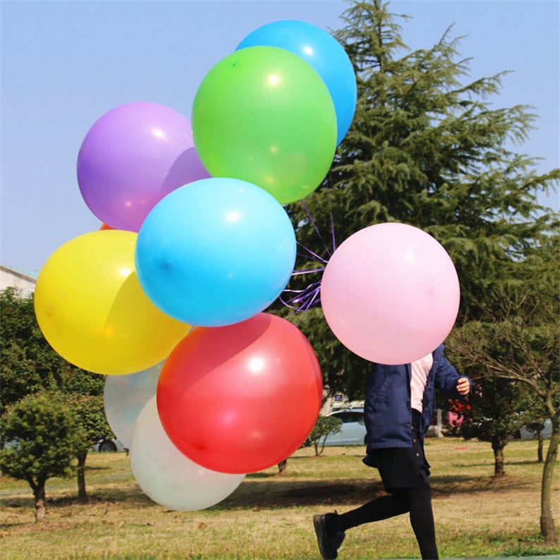 Op de afbeelding: Een groep kleurrijke ballonnen in verschillende tinten paars, groen, blauw, geel, roze en rood. De ballonnen zijn aan elkaar gebonden en worden vastgehouden door een persoon.