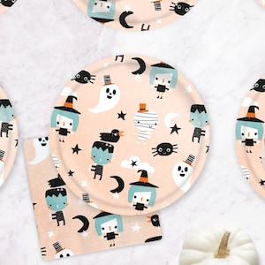 May include: A set of Halloween-themed paper plates and a napkin with a light peach background. The plates and napkin feature cartoon illustrations of ghosts, witches, spiders, and other spooky characters. The plates are round, and the napkin is square.