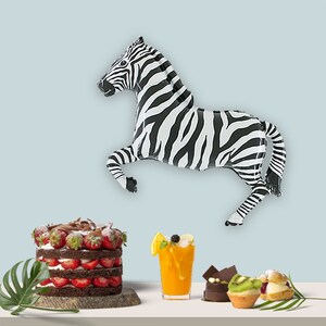 May include: A black and white zebra balloon, a chocolate cake with strawberries, a glass of orange juice, and a variety of pastries on a white table.