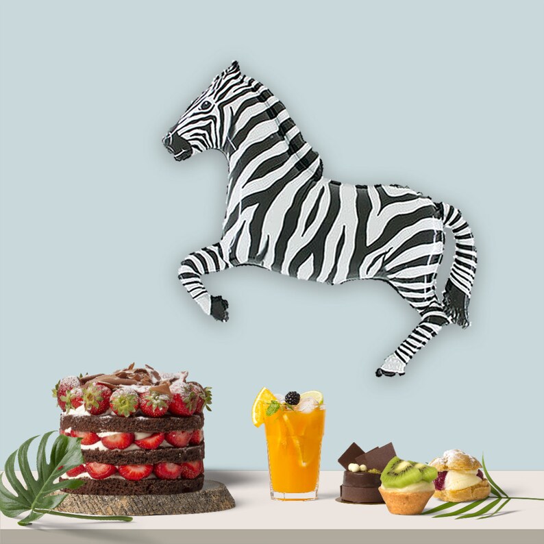 May include: A black and white zebra balloon, a chocolate cake with strawberries, a glass of orange juice, and a variety of pastries on a white table.