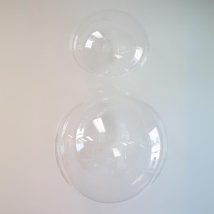 Op de afbeelding: Twee transparante plastic koepels, waarvan er &eacute;&eacute;n kleiner is dan de andere, zijn op elkaar gestapeld. De koepels zijn transparant en lijken van stevig plastic te zijn gemaakt.