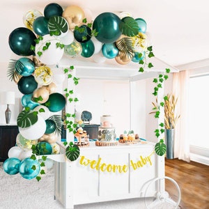 Op de afbeelding: Groene, gouden en witte ballonboog met groene bladeren en een gouden glitterbanner met de tekst "welcome baby".