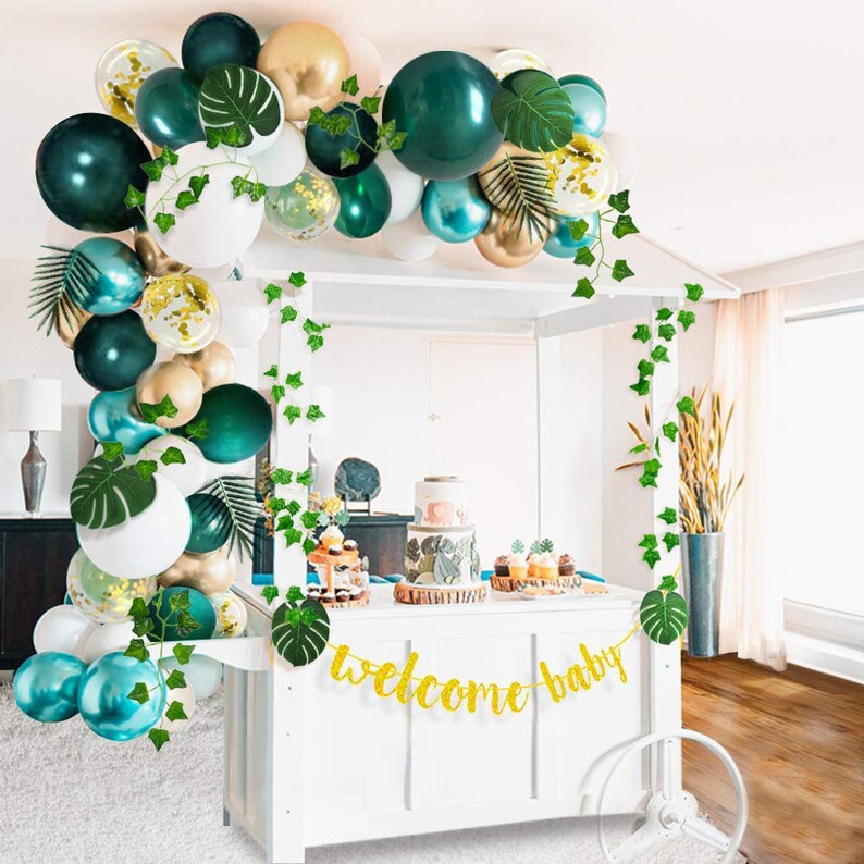Op de afbeelding: Groene, gouden en witte ballonboog met groene bladeren en een gouden glitterbanner met de tekst "welcome baby".