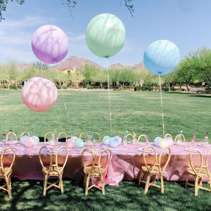 Puede incluir: Una mesa de fiesta con tem&aacute;tica pastel rosa y azul con globos, sillas y un mantel rosa.