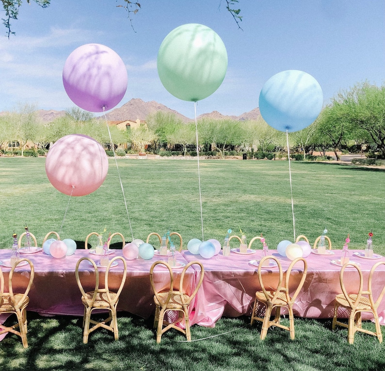 Puede incluir: Una mesa de fiesta con tem&aacute;tica pastel rosa y azul con globos, sillas y un mantel rosa.