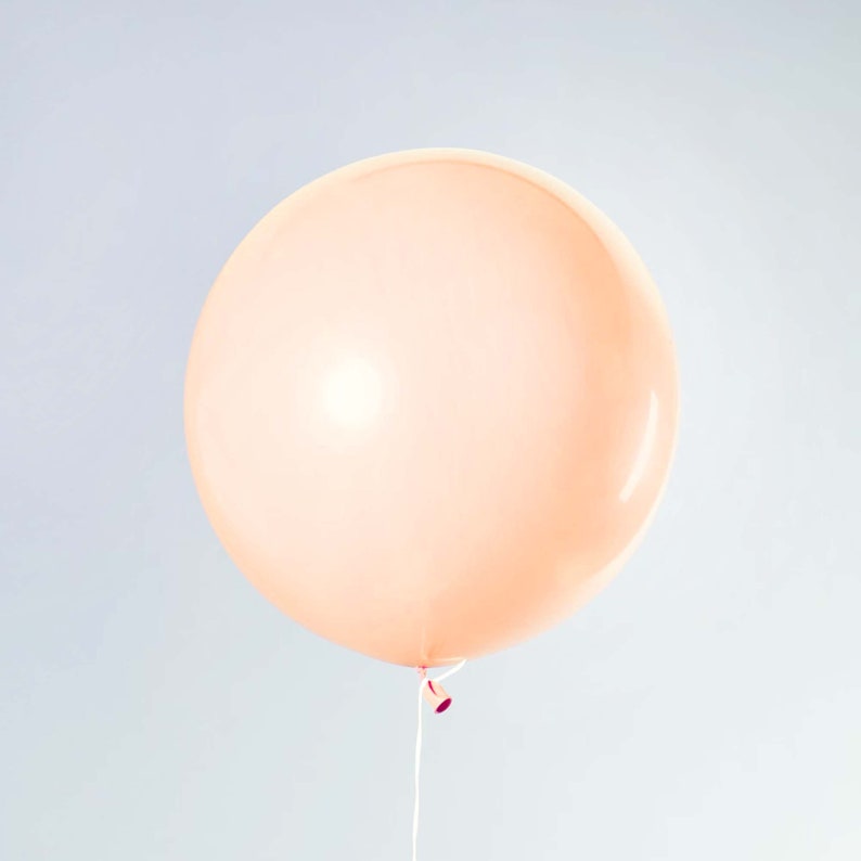 May include: A large, peach-colored balloon is inflated and tied with a string. The balloon is against a light gray background.