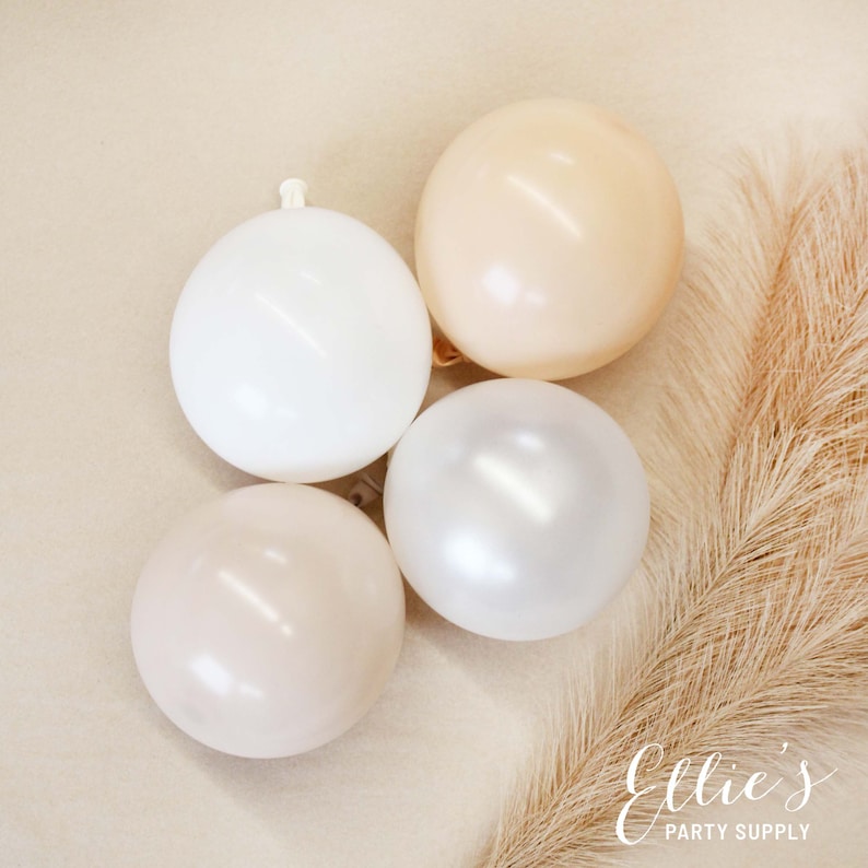 Może przedstawiać: Cztery balony w r&oacute;żnych odcieniach beżu, bieli i kremowego. Balony są ułożone w p&oacute;łkole na jasnobrązowym tle.