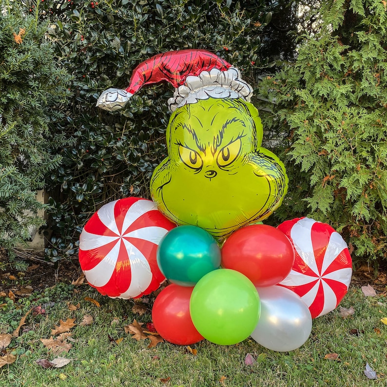 Pu&ograve; includere: Un palloncino verde del Grinch con un cappello rosso di Babbo Natale, circondato da palloncini a forma di bastoncino di zucchero rosso e bianco, palloncini verdi, rossi, bianchi e argentati.