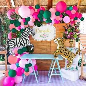 May include: A jungle-themed party decoration with pink, green, and white balloons, a zebra and tiger balloon animal, and a sign that says "Camila".