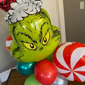 Pu&ograve; includere: Un palloncino verde Grinch con un cappello di Babbo Natale bianco, circondato da palloncini a forma di bastoncino di zucchero rosso e bianco e un palloncino verde, rosso e argento.