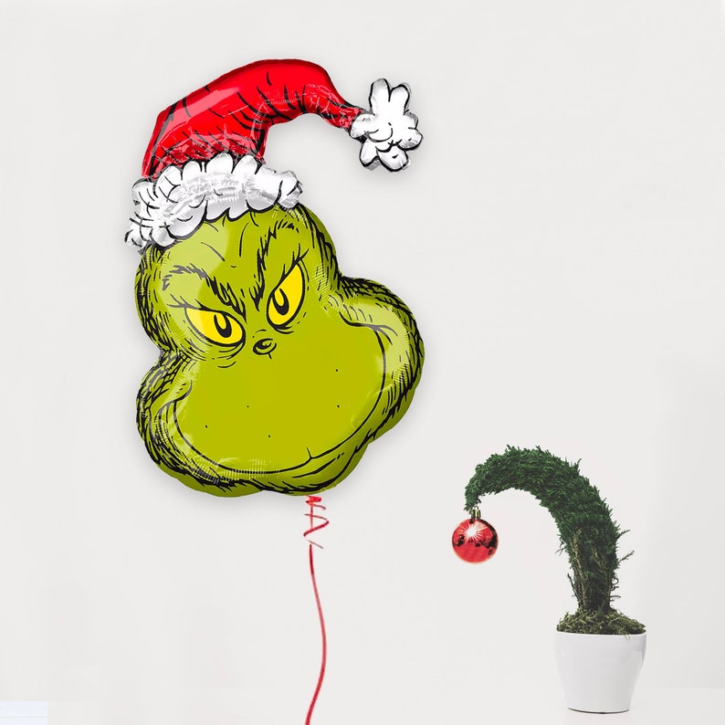 Pu&ograve; includere: Pallone verde del Grinch con un cappello di Babbo Natale rosso e bianco. Il pallone &egrave; legato a una corda e c'&egrave; un piccolo ornamento rosso appeso a un cespuglio verde.