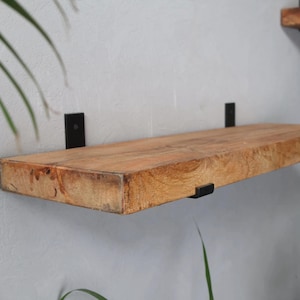 Może przedstawiać: Drewniana półka z naturalnym wykończeniem i czarnymi metalowymi wspornikami. Półka jest zamontowana na ścianie.