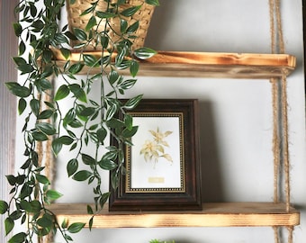 May include: Two wooden shelves with rope hangers, decorated with potted plants and a framed botanical print. The shelves are made of rustic wood with a natural finish.