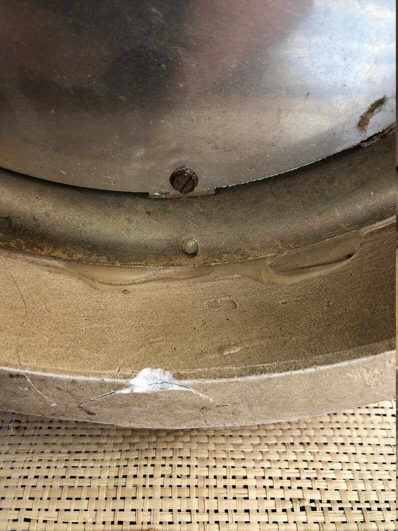 Puede incluir: Primer plano de la parte inferior de un reloj redondo de color plateado con un peque&ntilde;o tornillo visible. El reloj est&aacute; sobre una superficie tejida.