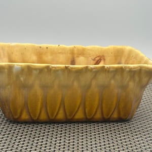 May include: A yellow ceramic planter with a scalloped rim and a textured design of vertical lines. The planter is rectangular and has a slightly rounded bottom.