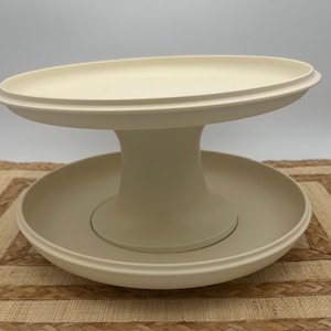 May include: A two-tiered white serving stand with a round top and bottom. The stand is made of a smooth, white plastic and has a simple, modern design.