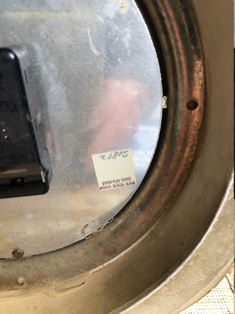 Puede incluir: La parte posterior de un reloj redondo plateado con un anillo exterior marr&oacute;n. El reloj tiene una pegatina que dice "TICK TOCK SHOP (403) 425-8585" y un n&uacute;mero escrito a mano "7086.2".