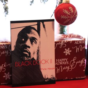 K&ouml;nnte beinhalten: Ein Schwarzwei&szlig;foto eines Mannes auf dem Cover eines Buches mit dem Titel "Black Book II" von Mose Hardin. Das Buch liegt auf einer roten Oberfl&auml;che mit einem roten Weihnachtsbaumschmuck und einer verpackten Geschenkbox mit einer wei&szlig;en Schneeflocke und den Worten "Happy Always Merry Everything" in wei&szlig;er Kursivschrift.