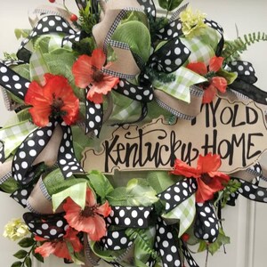 May include: A green, black, and white polka dot wreath with red poppy flowers and a sign that reads "My Old Kentucky Home".