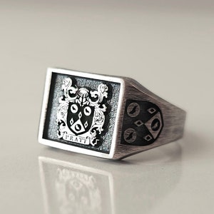 May include: A silver signet ring with a black and white coat of arms featuring a crest and the word "PRATT".