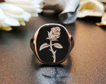 May include: A silver signet ring with a black onyx stone featuring an engraved rose design.