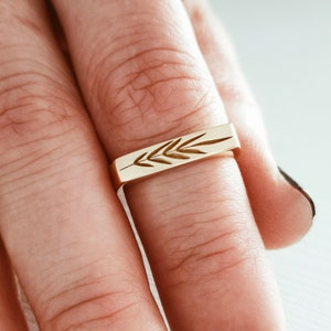 May include: A gold band ring with a delicate leaf design engraved on the top.