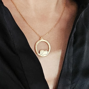 K&ouml;nnte beinhalten: Eine goldene Halskette mit einem runden Anh&auml;nger, der eine Silhouette eines Elefanten zeigt. Der Anh&auml;nger hat einen strukturierten Rand.
