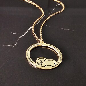 K&ouml;nnte beinhalten: Goldkette mit einem runden Anh&auml;nger, der eine Elefanten-Silhouette und die Inschrift "Wir waren einst Kinder, aber nur wenige von uns erinnern sich an 1975" zeigt.