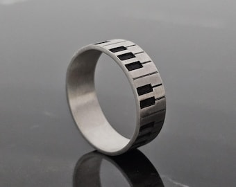 May include: A silver ring with a black piano key design. The ring is made of metal and has a polished finish.