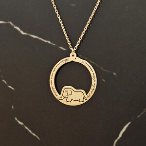 K&ouml;nnte beinhalten: Goldkette mit einem runden Anh&auml;nger, der eine Elefanten-Silhouette und die Inschrift "Alle Kinder werden entfernt... aber nur die Weisen erinnern sich an sie" zeigt.