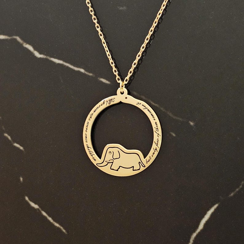 K&ouml;nnte beinhalten: Goldkette mit einem runden Anh&auml;nger, der eine Elefanten-Silhouette und die Inschrift "Alle Kinder werden entfernt... aber nur die Weisen erinnern sich an sie" zeigt.