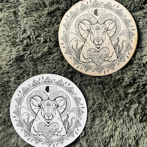 May include: Two wooden coasters with a black and white illustration of a ram with a heart that says "Billy Strings" inside. The ram is surrounded by a circular design of musical notes and geometric shapes.