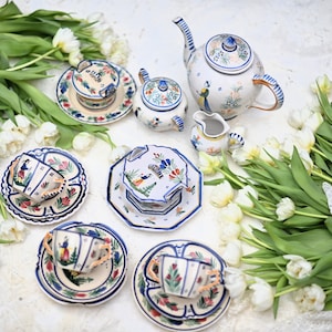 May include: A set of blue and white ceramic teacups, saucers, and a teapot with a floral design. The teapot has a peacock design on the side. The set is surrounded by white tulips.