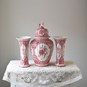 Puede incluir: Tres jarrones de porcelana roja y blanca con diseños florales. El jarrón del centro tiene una tapa con una pequeña figura en la parte superior.