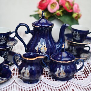 May include: A blue and gold tea set with a teapot, creamer, sugar bowl, and four cups and saucers. The set is decorated with a white floral design and gold accents.