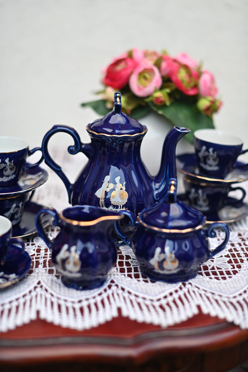 May include: A blue and gold tea set with a teapot, creamer, sugar bowl, and four cups and saucers. The set is decorated with a white floral design and gold accents.