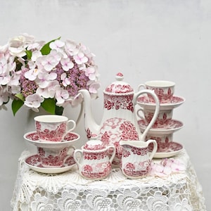 Könnte beinhalten: Ein Vintage-Tee-Set mit einem roten und weißen Blumenmuster. Das Set enthält eine Teekanne, eine Milchkännchen, eine Zuckerdose und vier Teetassen und Untertassen.