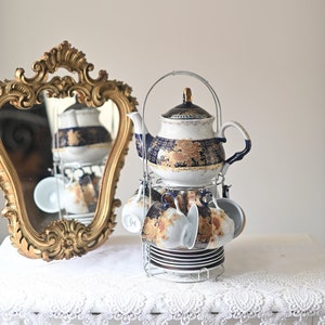 May include: A porcelain tea set with a blue and gold floral design. The set includes a teapot, cups, and saucers, all arranged on a metal stand.