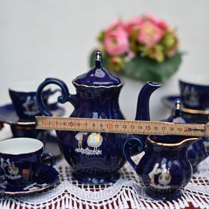 May include: A blue and gold tea set with a teapot, creamer, sugar bowl, and two cups and saucers. The set features a delicate floral design and is displayed on a white lace tablecloth.